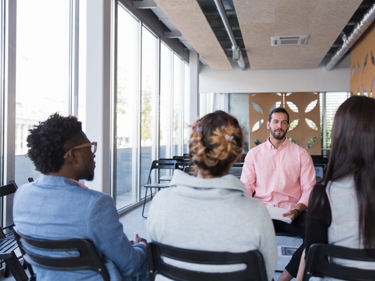 Un formateur échange avec un petit groupe de participants assis, lors d'une session de formation en salle.